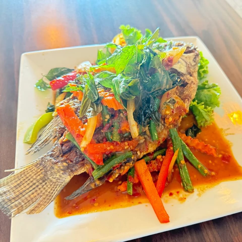 Whole fried fish with red chili sauce, green beans, carrots, and basil on a white plate.