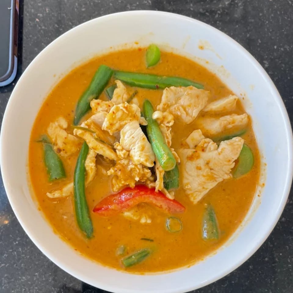 Close-up of a bowl of Thai red curry with chicken, green beans, and red bell pepper.