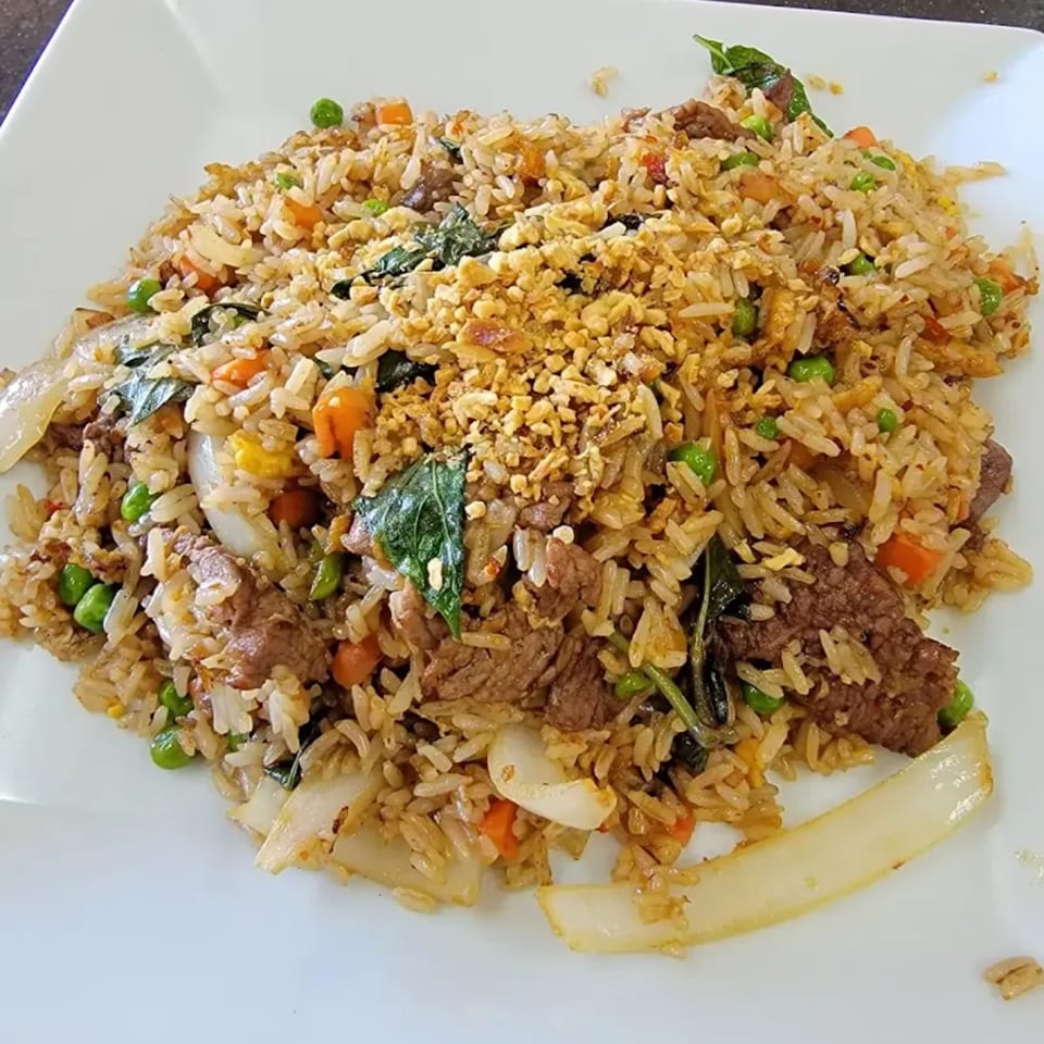 Thai fried rice with beef, peas, carrots, onions, basil, and crispy garlic on a white plate.