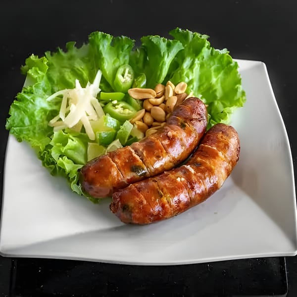Two grilled Thai sausages with lettuce, sliced peppers, ginger, and peanuts on a white plate.