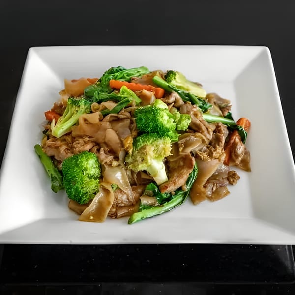 Pad See Ew with wide rice noodles, beef, broccoli, carrots, and Chinese broccoli on a white plate.