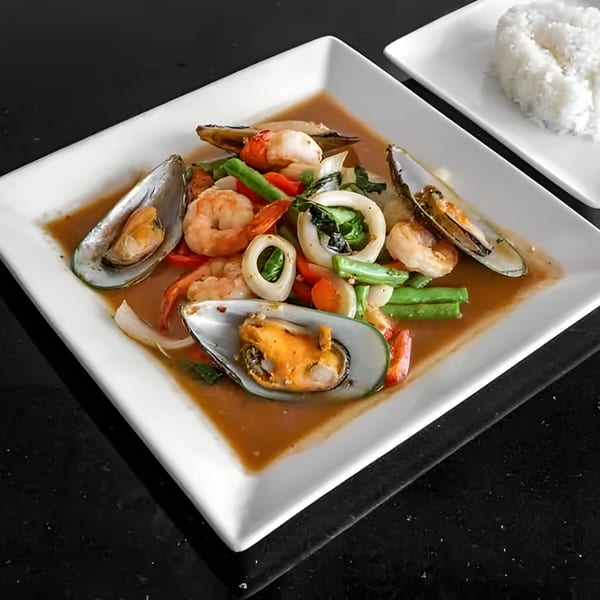 Thai seafood dish with mussels, shrimp, squid, and vegetables in a savory sauce, served with rice.