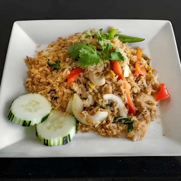 Thai fried rice with chicken, vegetables, and cilantro, garnished with cucumber slices.